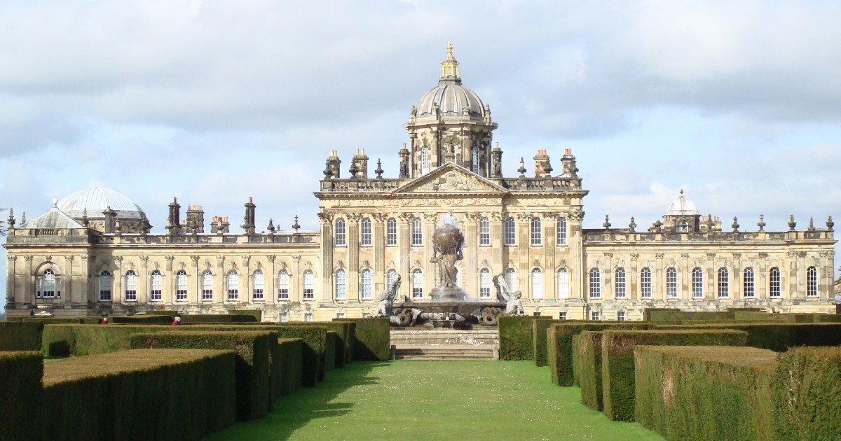 Castle Howard, a vast baroque stately home with a domed and pedimented central block and wings on either side, with formal box hedges in the foreground